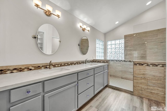 bathroom with a tile shower, vanity, hardwood / wood-style flooring, tile walls, and lofted ceiling