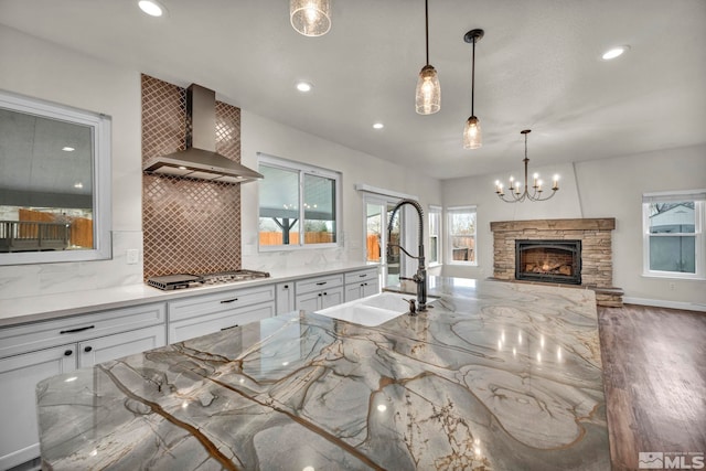 kitchen featuring stainless steel gas stovetop, wall chimney range hood, sink, decorative backsplash, and white cabinetry