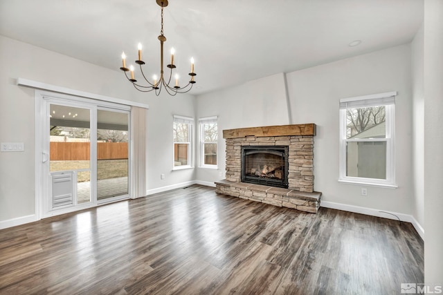 unfurnished living room with a stone fireplace, a wealth of natural light, dark hardwood / wood-style floors, and a notable chandelier