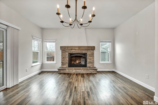 unfurnished living room featuring a stone fireplace, dark wood-type flooring, and a chandelier