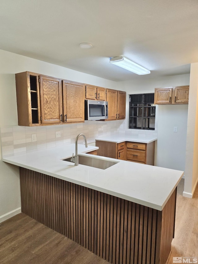 kitchen featuring tasteful backsplash, kitchen peninsula, sink, and light wood-type flooring