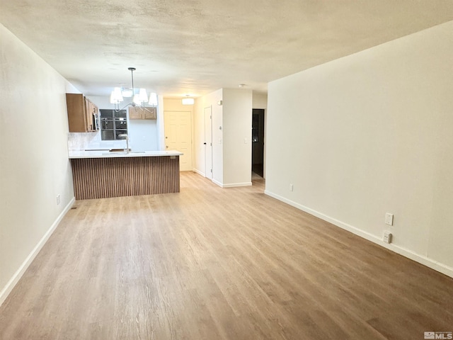 kitchen featuring kitchen peninsula, tasteful backsplash, wood-type flooring, a chandelier, and hanging light fixtures