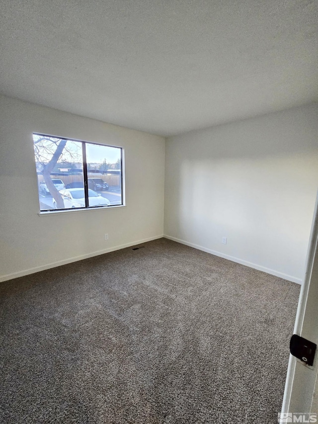 spare room featuring dark colored carpet and a textured ceiling