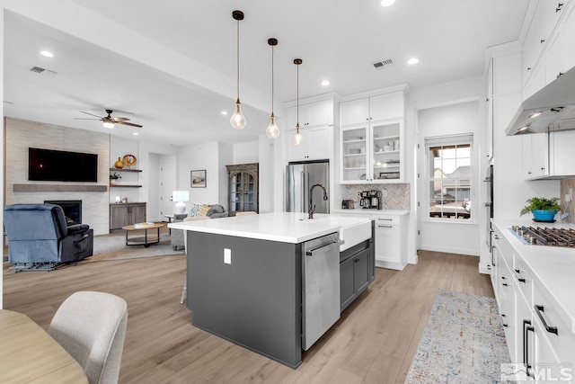 kitchen featuring stainless steel appliances, extractor fan, a kitchen island with sink, sink, and white cabinetry