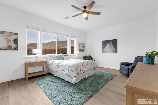 bedroom with a mountain view, light wood-type flooring, and ceiling fan