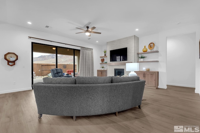 living room featuring ceiling fan, a fireplace, and light hardwood / wood-style flooring