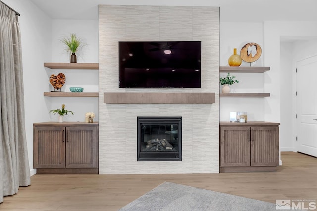 living room with light hardwood / wood-style floors, built in features, and a tiled fireplace