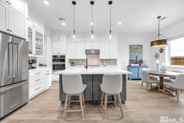 kitchen featuring a kitchen island with sink, white cabinets, hanging light fixtures, decorative backsplash, and stainless steel appliances