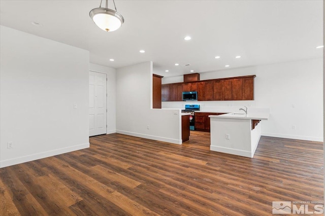 kitchen featuring sink, dark hardwood / wood-style flooring, stainless steel range oven, a kitchen bar, and a center island with sink