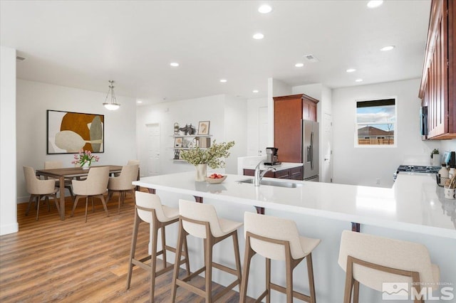 kitchen with sink, range with gas cooktop, stainless steel refrigerator with ice dispenser, kitchen peninsula, and decorative light fixtures