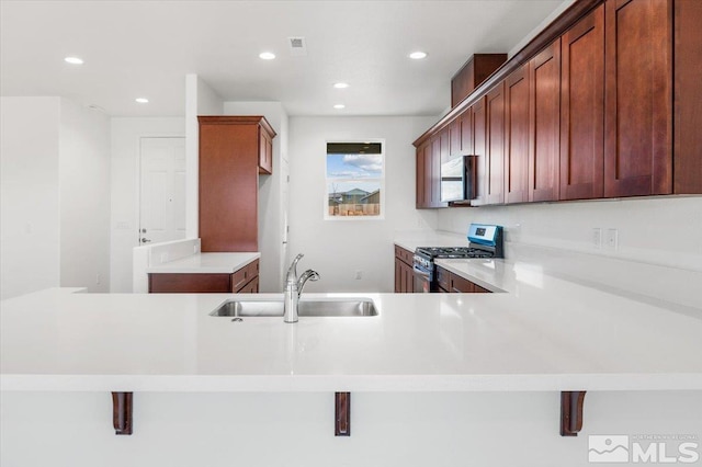 kitchen featuring stainless steel gas stove, a kitchen breakfast bar, kitchen peninsula, and sink