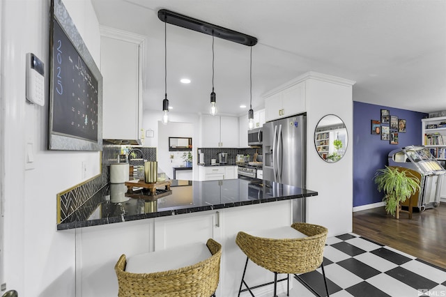 kitchen featuring a kitchen breakfast bar, backsplash, stainless steel appliances, pendant lighting, and white cabinetry