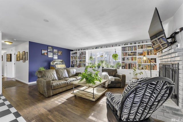 living room featuring built in shelves, hardwood / wood-style flooring, and a brick fireplace