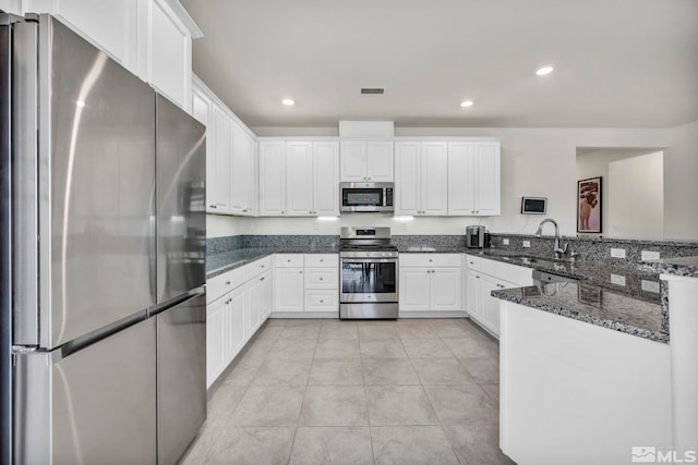 kitchen with stainless steel appliances, sink, light tile patterned floors, dark stone countertops, and white cabinets