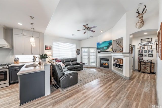 living room featuring vaulted ceiling, ceiling fan, sink, a fireplace, and light hardwood / wood-style floors