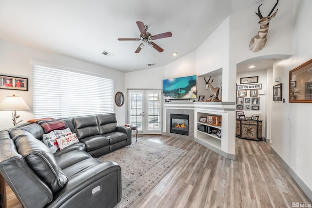 living room featuring ceiling fan, light wood-type flooring, a fireplace, and vaulted ceiling