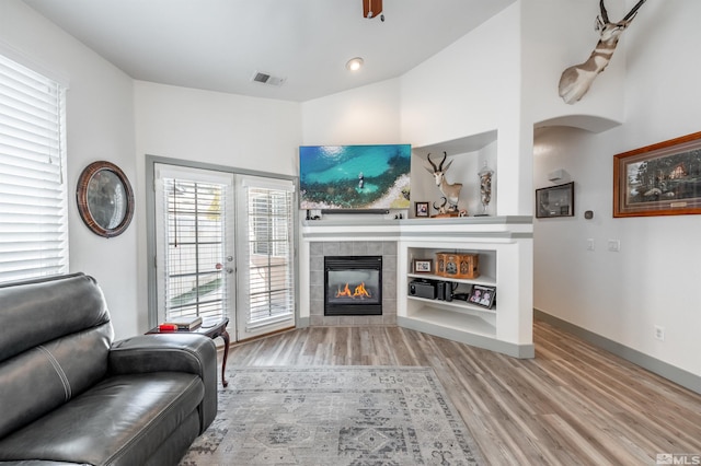 living room with french doors, ceiling fan, a fireplace, light hardwood / wood-style floors, and lofted ceiling