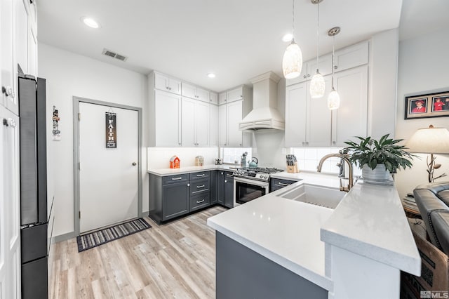 kitchen with custom exhaust hood, stainless steel appliances, sink, decorative light fixtures, and gray cabinets