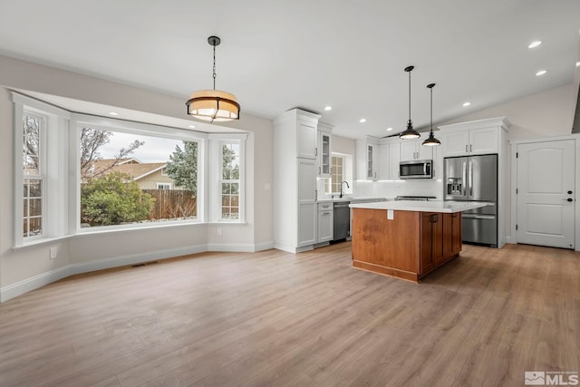 kitchen featuring white cabinets, appliances with stainless steel finishes, a kitchen island, and hanging light fixtures