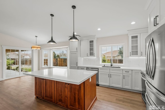 kitchen with white cabinetry, hanging light fixtures, backsplash, a kitchen island, and appliances with stainless steel finishes