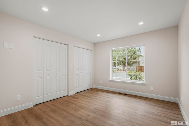 unfurnished bedroom with light hardwood / wood-style flooring and multiple closets