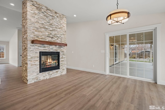 unfurnished living room with lofted ceiling, light hardwood / wood-style flooring, a stone fireplace, and a healthy amount of sunlight