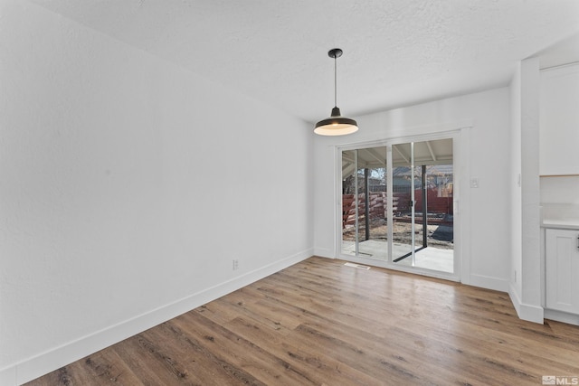 unfurnished dining area with a textured ceiling and light wood-type flooring