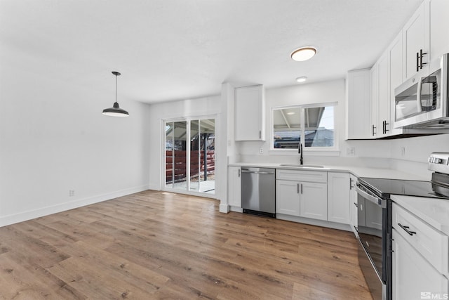 kitchen with appliances with stainless steel finishes, sink, pendant lighting, hardwood / wood-style floors, and white cabinetry