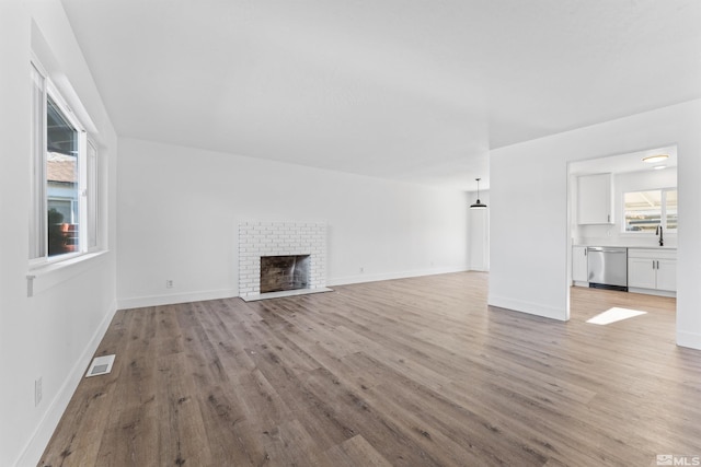 unfurnished living room with light wood-type flooring, sink, and a brick fireplace