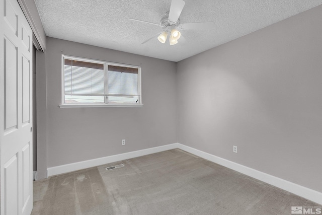 empty room with ceiling fan, light colored carpet, and a textured ceiling