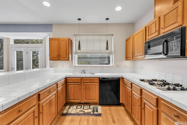 kitchen featuring black appliances, sink, decorative light fixtures, tile counters, and light hardwood / wood-style floors