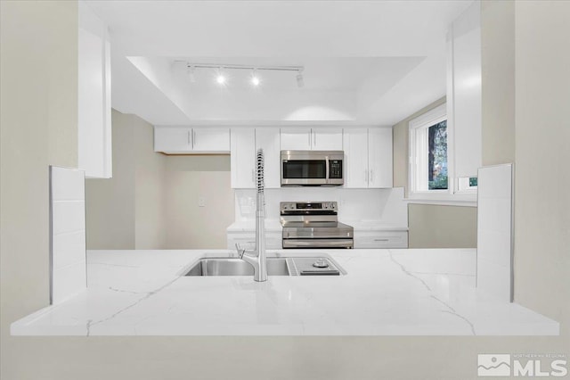 kitchen with light stone counters, white cabinetry, stainless steel appliances, and track lighting