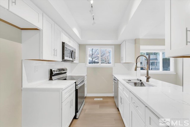 kitchen featuring sink, light stone countertops, light wood-type flooring, white cabinetry, and stainless steel appliances