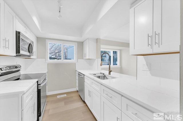 kitchen with white cabinets, appliances with stainless steel finishes, light stone countertops, and sink