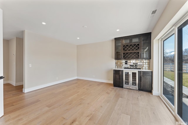 bar with light wood-type flooring, wine cooler, and tasteful backsplash