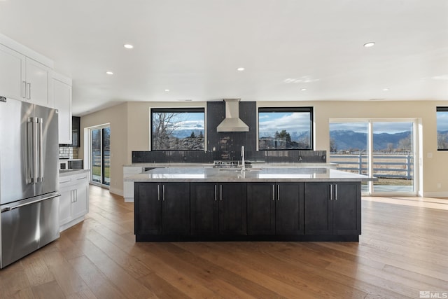 kitchen with white cabinets, a spacious island, wall chimney range hood, light stone countertops, and high quality fridge