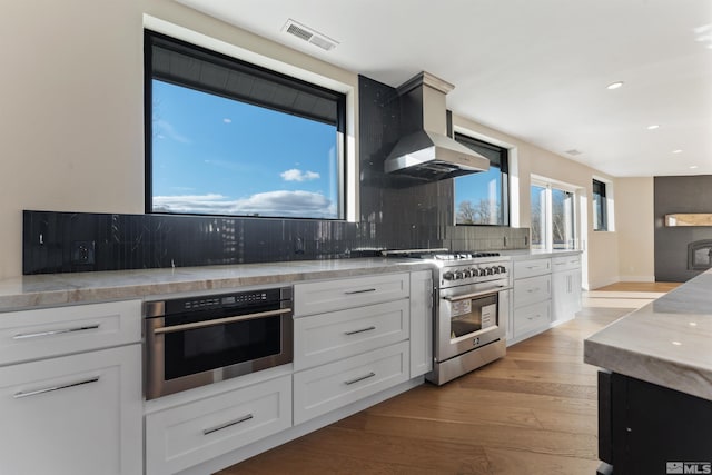 kitchen featuring light hardwood / wood-style flooring, wall chimney exhaust hood, decorative backsplash, white cabinetry, and stainless steel appliances