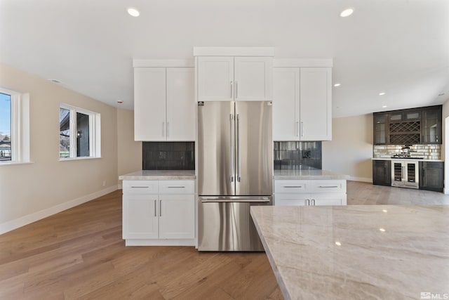 kitchen featuring backsplash, white cabinets, light hardwood / wood-style floors, light stone counters, and stainless steel refrigerator