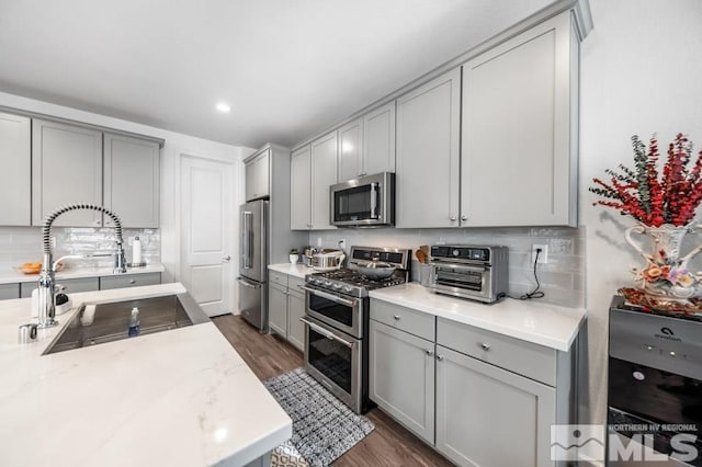 kitchen featuring gray cabinetry, sink, stainless steel appliances, dark wood-type flooring, and backsplash