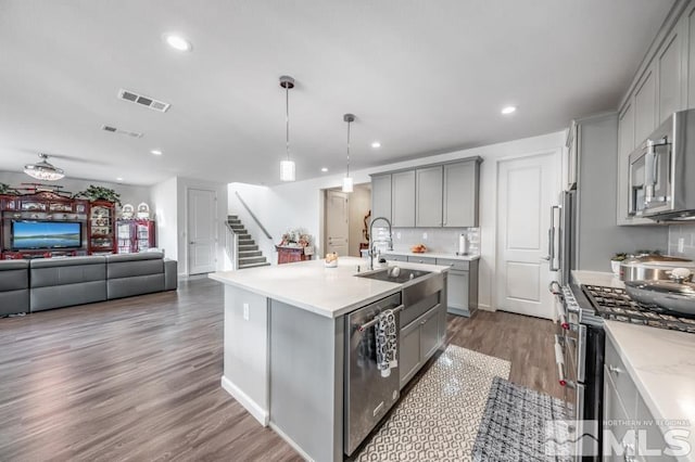 kitchen featuring sink, stainless steel appliances, decorative light fixtures, gray cabinets, and a center island with sink