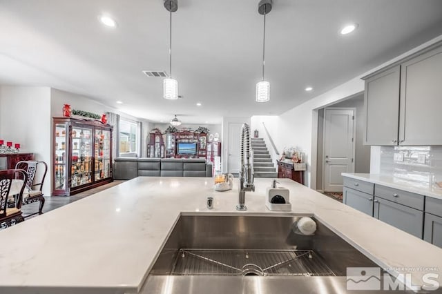 kitchen with gray cabinets, light stone counters, a kitchen island, and hanging light fixtures