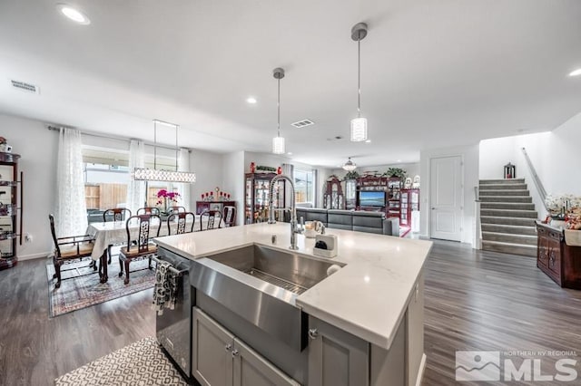 kitchen with gray cabinetry, dishwasher, sink, hanging light fixtures, and a center island with sink