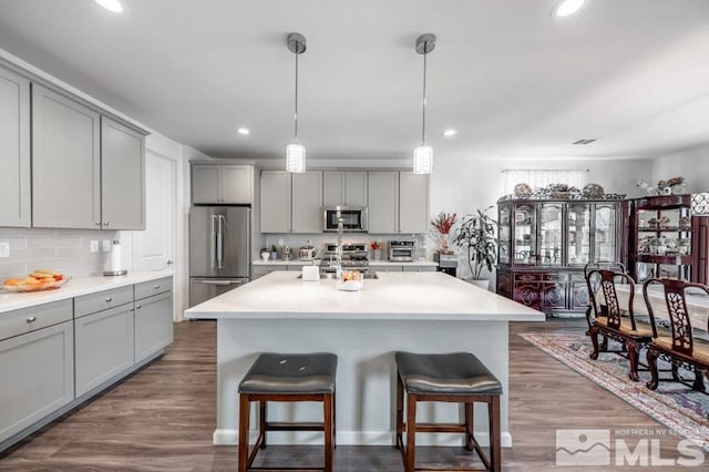 kitchen featuring gray cabinetry, hanging light fixtures, a kitchen island with sink, and appliances with stainless steel finishes