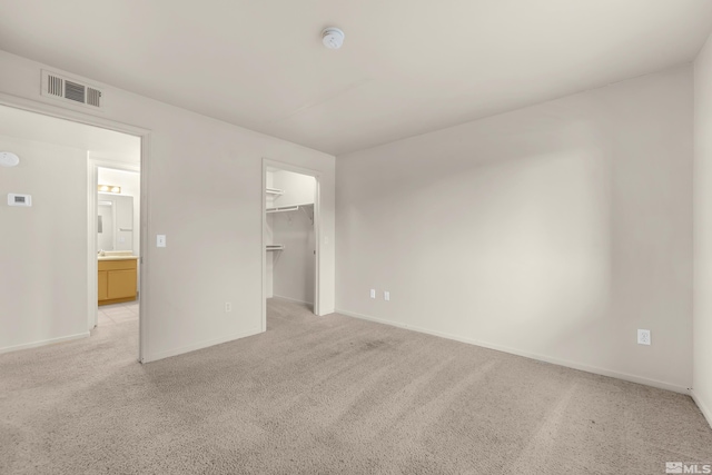 unfurnished bedroom featuring a walk in closet, a closet, and light colored carpet