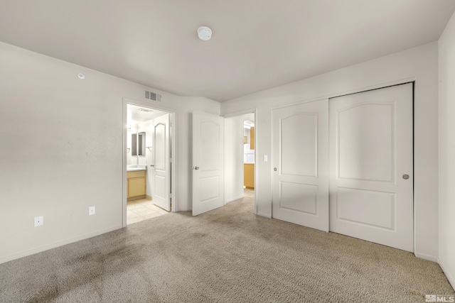 unfurnished bedroom featuring a closet, light colored carpet, and ensuite bath