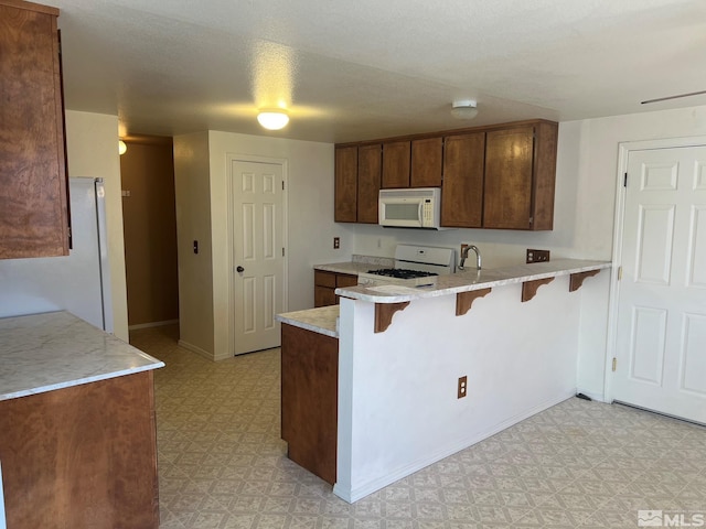 kitchen with sink, kitchen peninsula, a textured ceiling, white appliances, and a kitchen bar