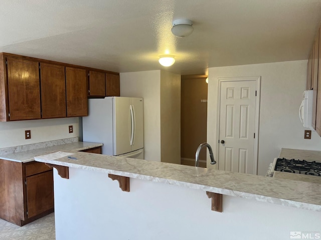 kitchen with a kitchen bar, kitchen peninsula, a textured ceiling, white appliances, and sink