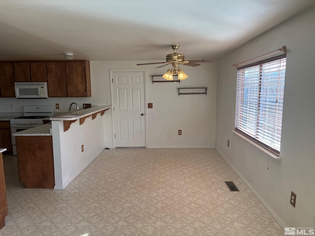 kitchen featuring kitchen peninsula, white appliances, ceiling fan, sink, and a breakfast bar area