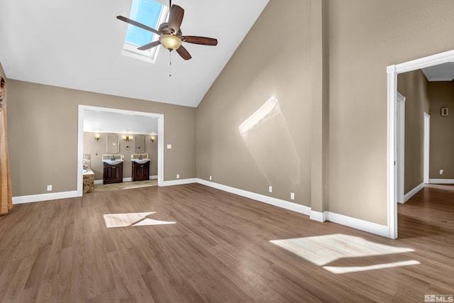 unfurnished living room with high vaulted ceiling, sink, a skylight, hardwood / wood-style flooring, and ceiling fan