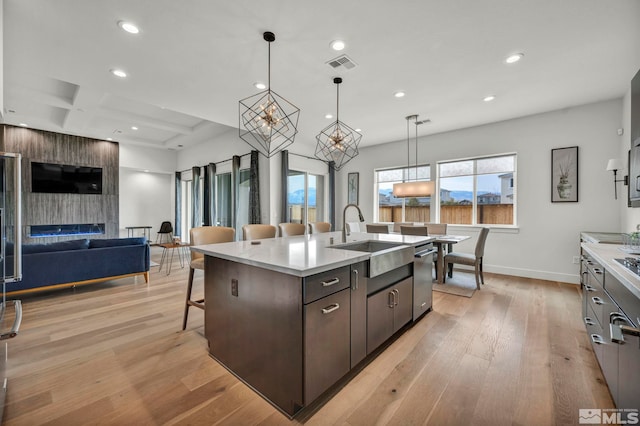 kitchen with dark brown cabinets, a kitchen island with sink, sink, decorative light fixtures, and light hardwood / wood-style floors